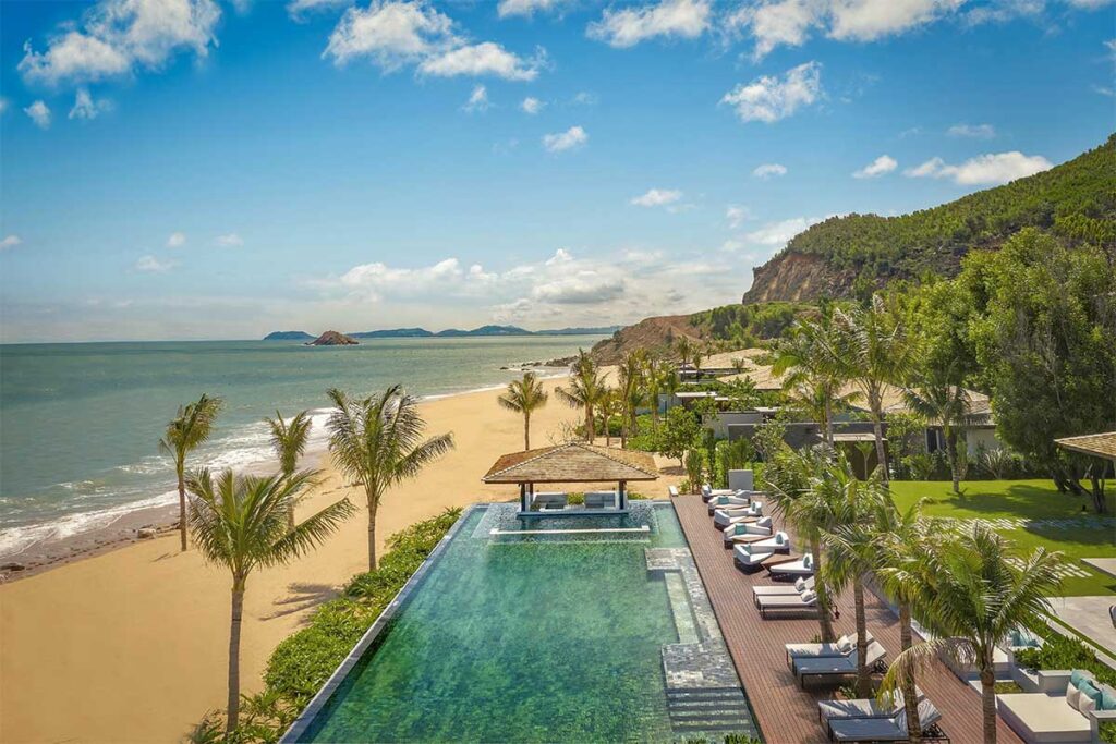 Luxury beachfront pool at Anantara Quy Nhon Villas, with palm trees, sun loungers, and a quiet golden beach along the South Central Coast of Vietnam.