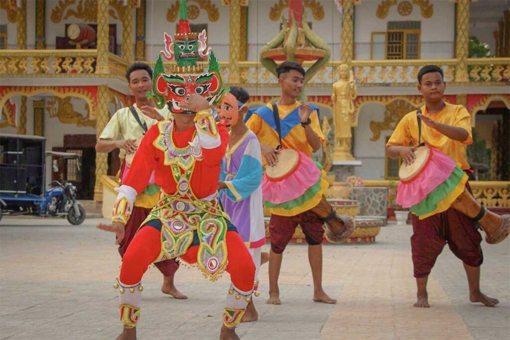Traditional Khmer dance performance during Chol Chnam Thmay in Vietnam, with young men in colorful costumes playing drums and a masked dancer in the foreground.
