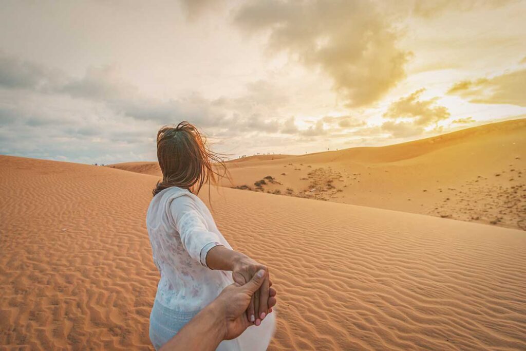 Couple walking hand in hand across the sand dunes in Mui Ne, one of Vietnam’s most romantic landscapes.