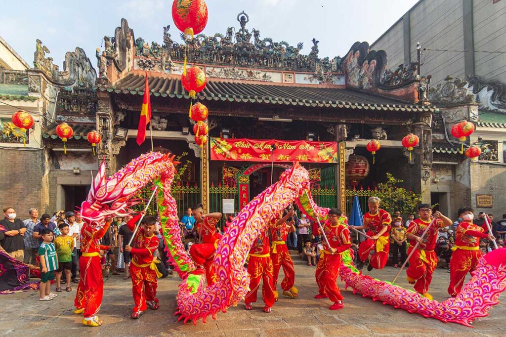 Traditional Vietnamese dragon dance performed in front of a Chinese temple during a festival, accompanied by drums and an audience.