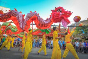 Vietnamese dragon dance performed during a street celebration, with dancers carrying a long red dragon costume through a crowded urban area.