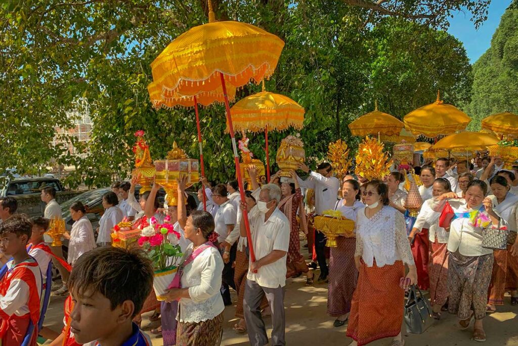 Procession of Buddhist followers carrying offerings with golden umbrellas during the Kathina Festival in Cambodia.