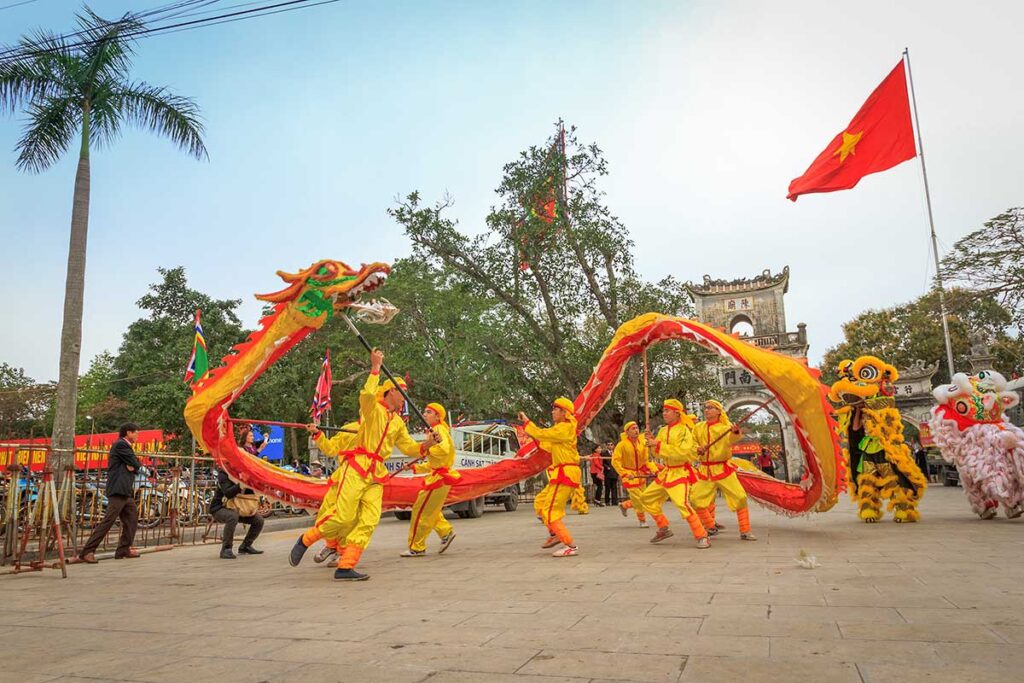 Vietnamese dragon dance performed in an open public square, with performers in yellow costumes and the national flag visible in the background.