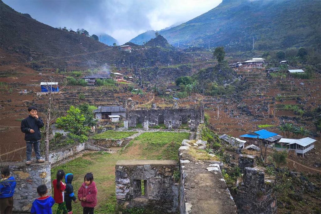 Children playing at the ruins of a French watch post in Ha Giang, with a mountain and village in the background.