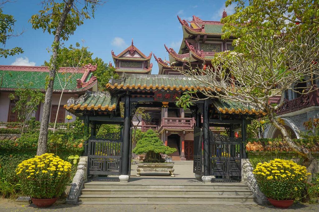 Entrance to Thien Hung Pagoda outside Quy Nhon, featuring traditional curved roofs, bonsai trees, and colorful temple architecture.