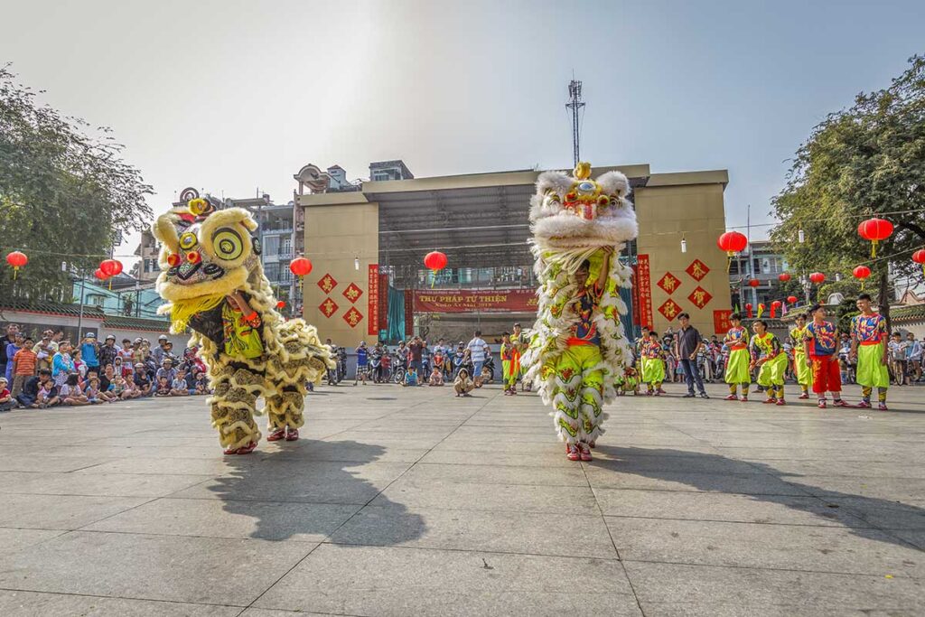 Traditional Vietnamese lion dance performance in an open public courtyard, watched by a large local audience.