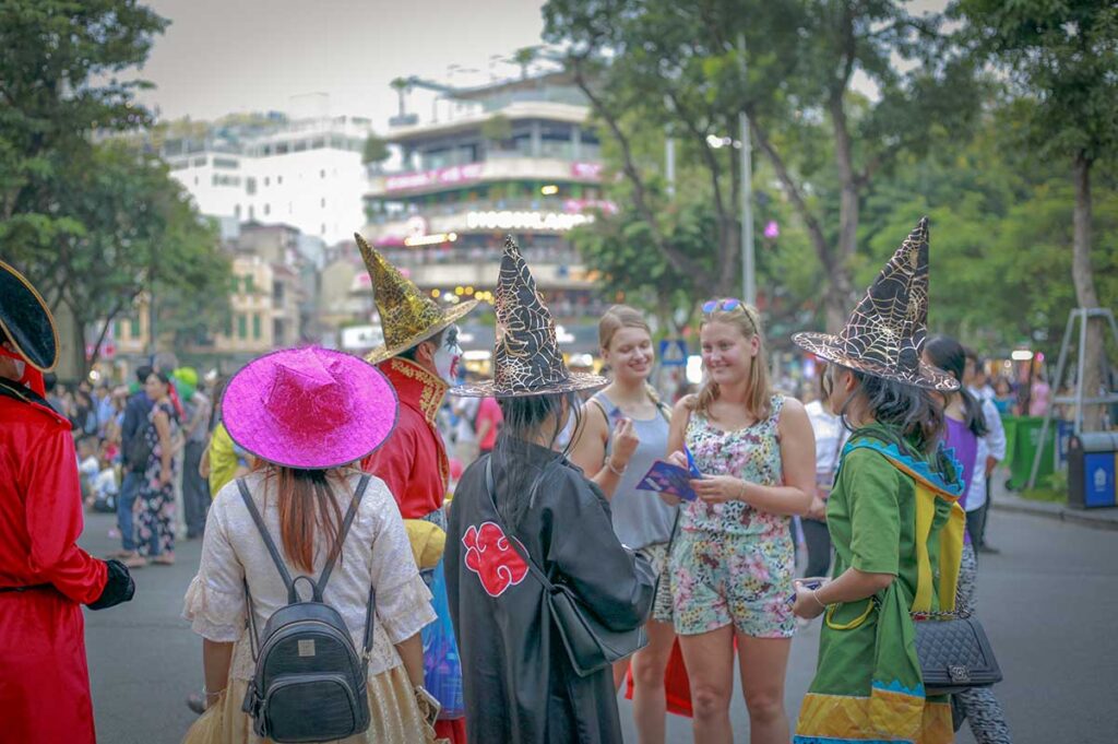 People wearing Halloween costumes and witch hats gathering in Hanoi Old Quarter during Halloween celebrations.