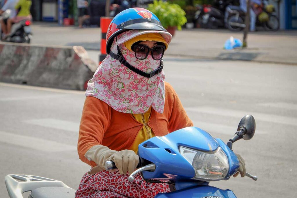 Vietnamese woman riding a motorbike wearing full face covering and mask for sun and dust protection