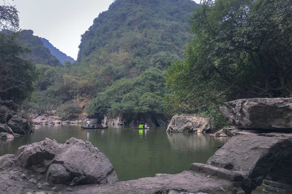 A boat going over a small lake between mountains at Ao Dong Tourist Area
