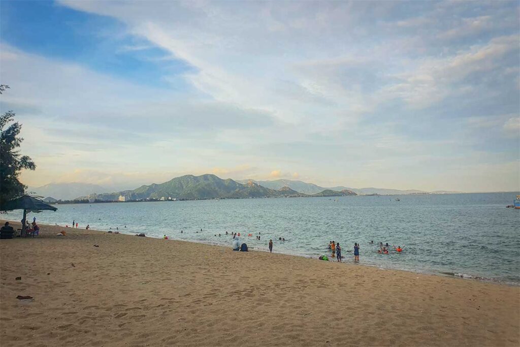 Binh Son Beach in Phan Rang with golden sand, calm waves, and families swimming against a backdrop of green mountains.