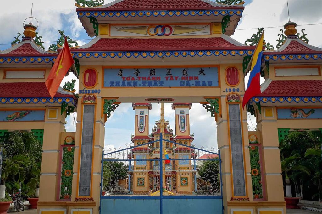 Colorful Cao Dai Temple in Ca Mau with ornate gate, red-tiled roofs, and bright religious symbols.