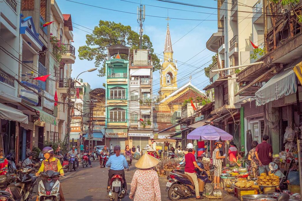 Busy street scene in Chinatown Ho Chi Minh City with motorbikes, street vendors and Cha Tam Church in the background