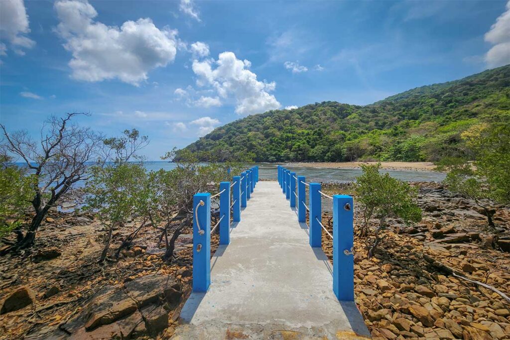 Concrete pier at Dat Tham Beach in Con Dao stretching into a rocky shoreline with calm sea and forest-covered hills in the background.