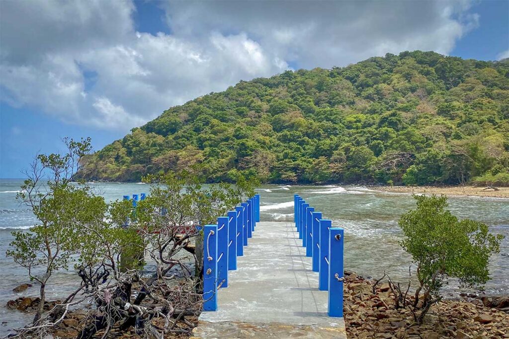 Concrete pier extending into the sea at Dat Tham Beach in Con Dao National Park, surrounded by rocky coastline and green hills in the background