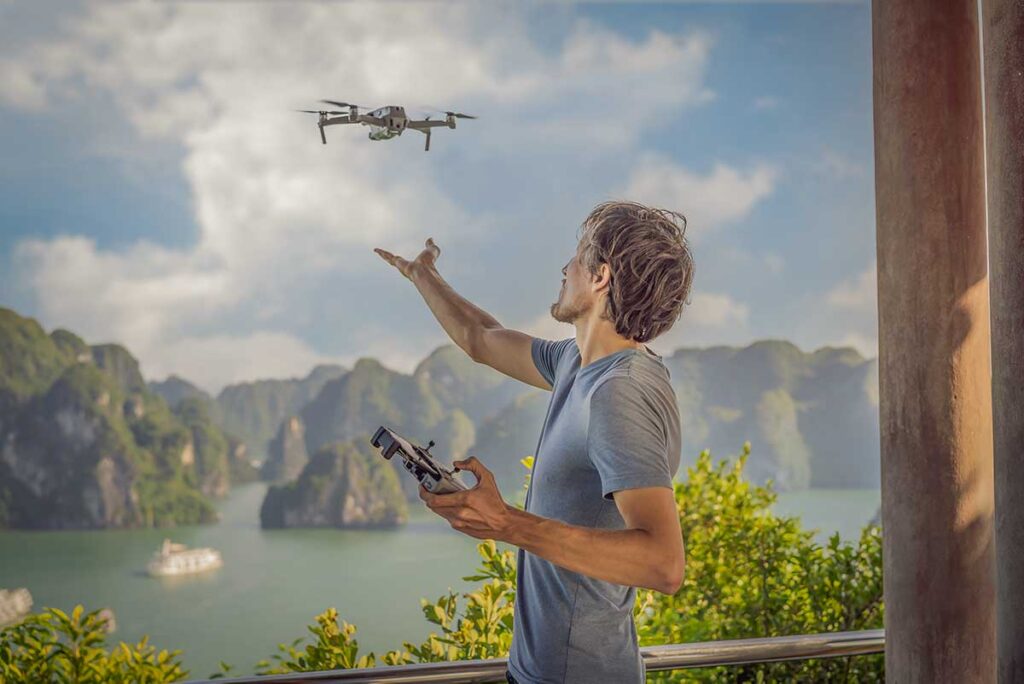 Man flying a drone over Ha Long Bay from a scenic viewpoint, with limestone islands and boats visible below