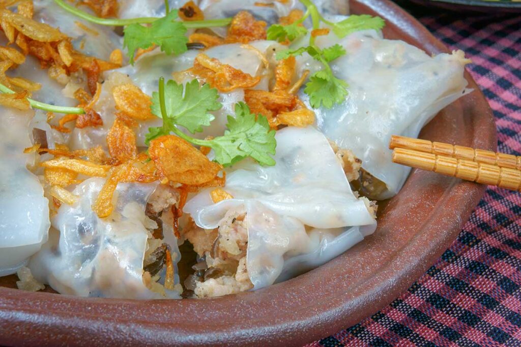 Plate of Vietnamese dumplings topped with crispy fried shallots and fresh herbs, served in a rustic bowl