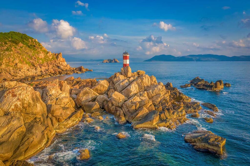 Ganh Den Lighthouse in Phu Yen, Vietnam, standing on rugged coastal rocks with panoramic sea views at sunset.