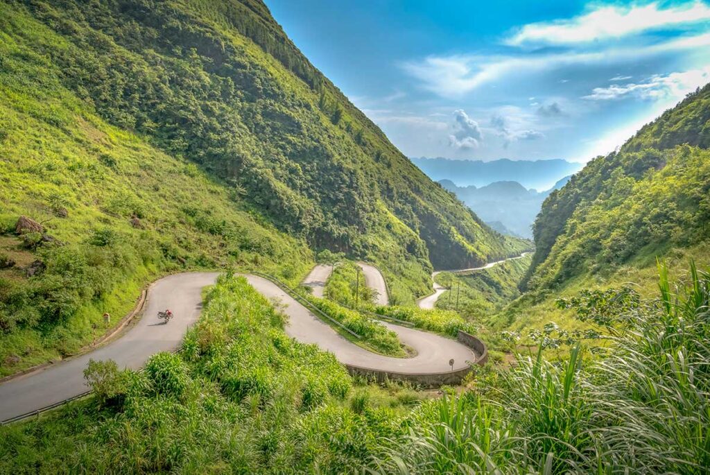 Winding mountain road at Tham Ma Pass in Ha Giang, surrounded by green hills and dramatic valleys, ideal for landscape photography