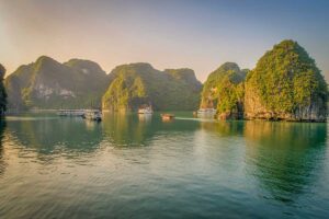 Halong Bay landscape with limestone islands and cruise boats on calm green water in soft morning light