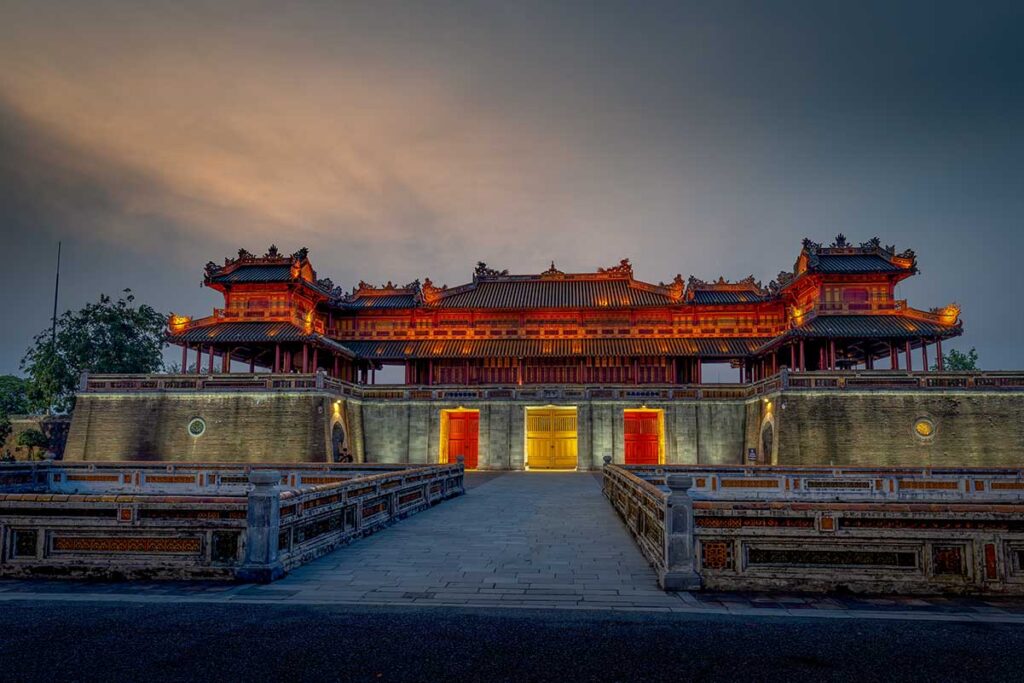 Imperial City gate in Hue illuminated at dusk, showing traditional Vietnamese architecture with warm lighting and a quiet entrance courtyard