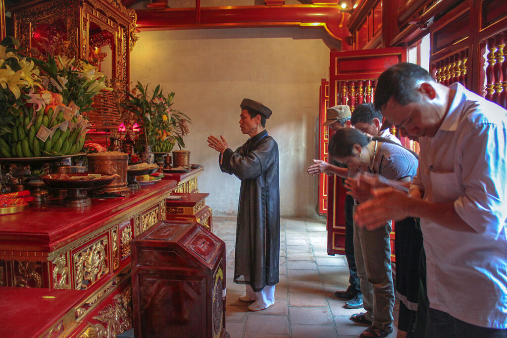 A man in traditional temple clothes is praying inside Trung Temple (Middle Temple) at Hung King Temple Complex