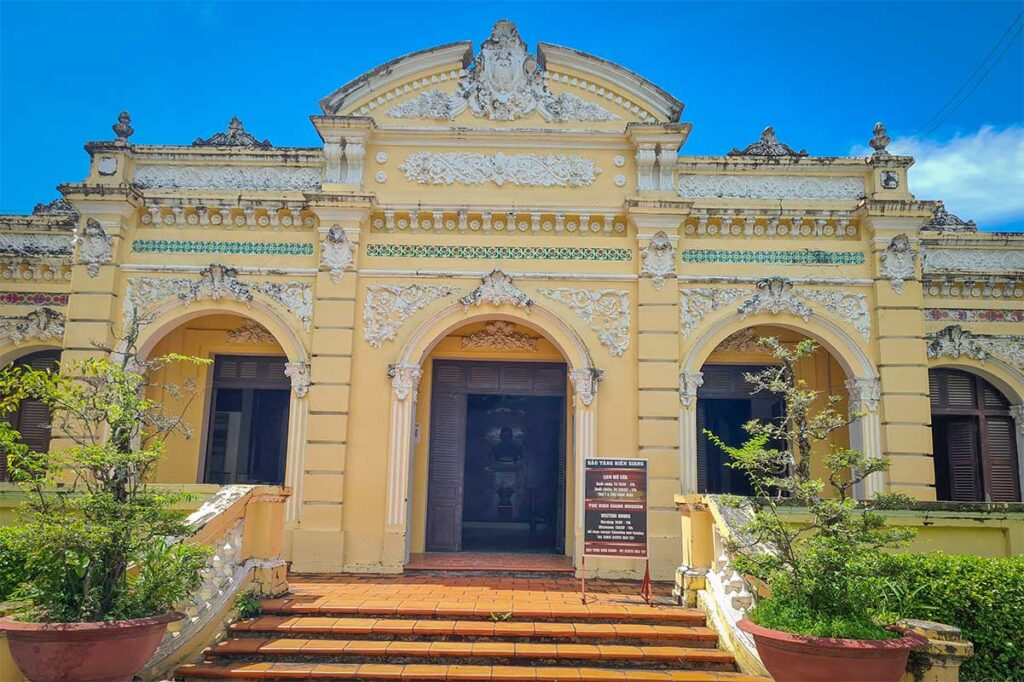 Front facade of Kien Giang Museum in Rach Gia, Vietnam, a colonial-era yellow building featuring ornate French-style architecture and arched entryways.