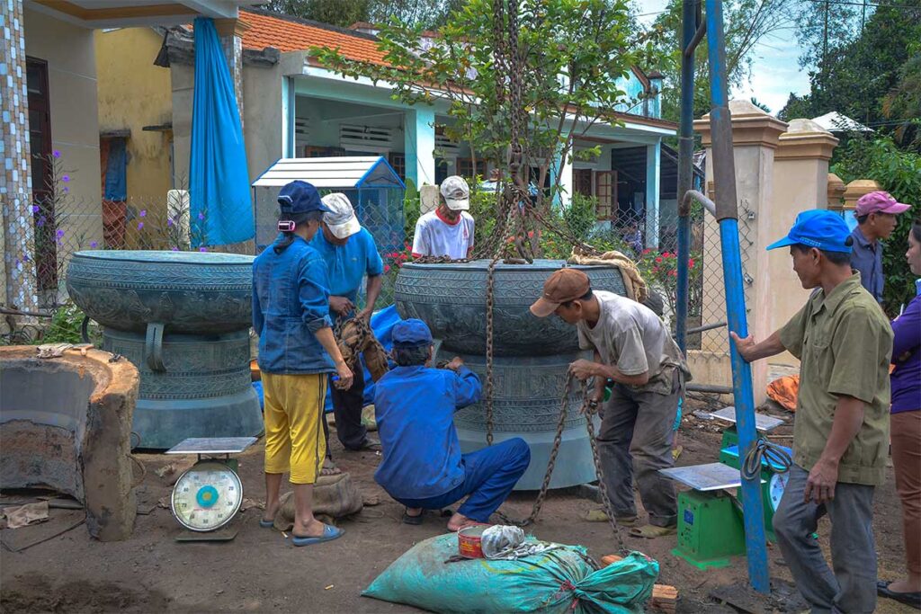 A few man are trying to move a huge bronze plant pot at Long Thuong Bronze Casting Village