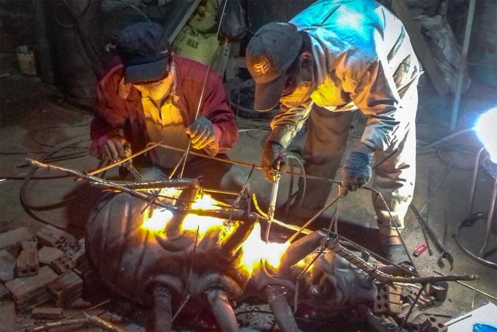 Two man building a bronze statue of an ant and use heat to melt parts together at Long Thuong Bronze Casting Village