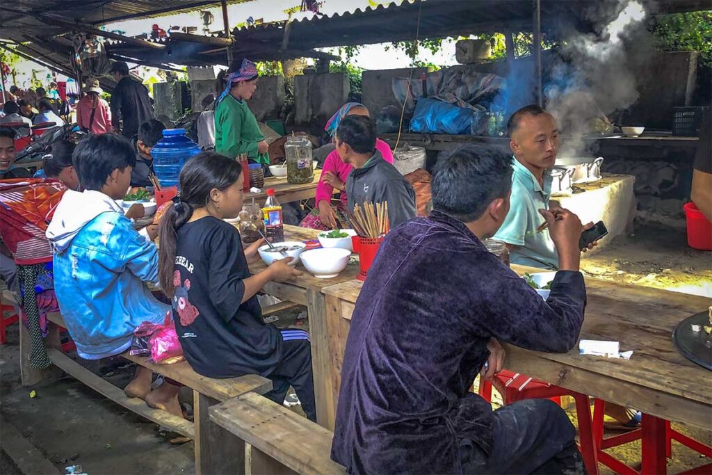Local ethnic minorities are enjoying a meal wiles sitting on long tables at the Lung Phin Market