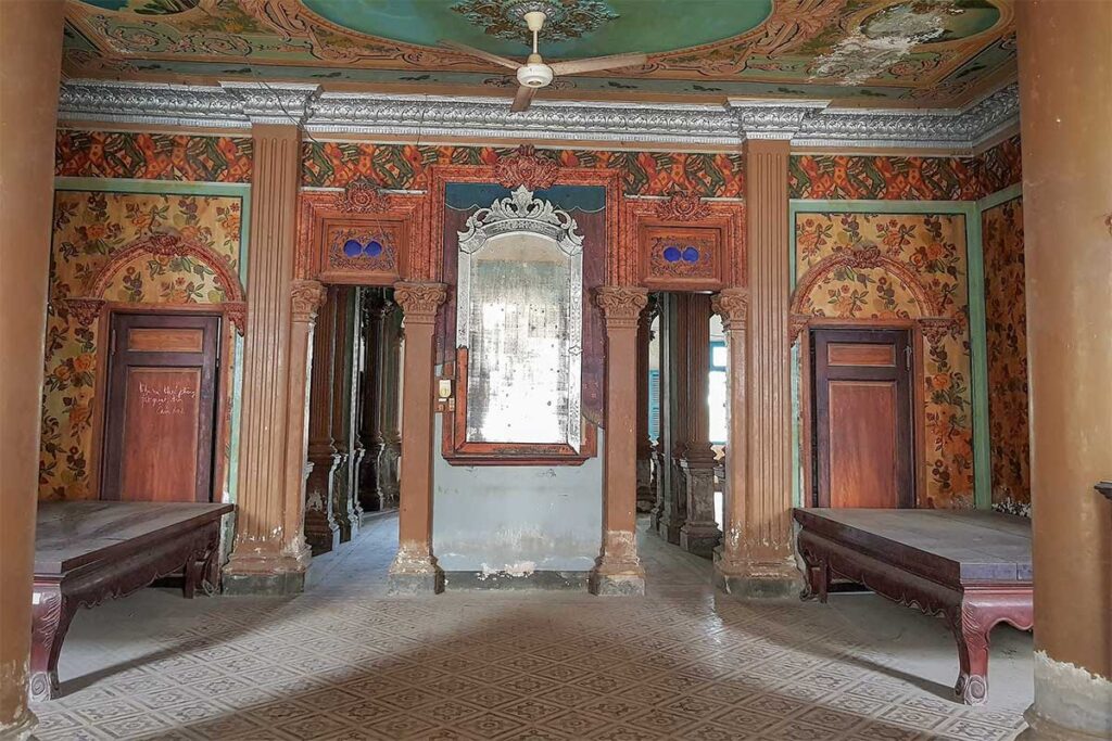 Colorful and faded interior of Huynh Ky Mansion, showcasing vintage wallpaper, painted ceilings, and antique wooden furniture in Tra Vinh.