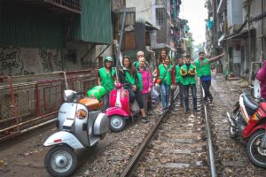 Group of travelers on Hanoi Train Street with Vespa motorbikes parked nearby during a motorbike tour