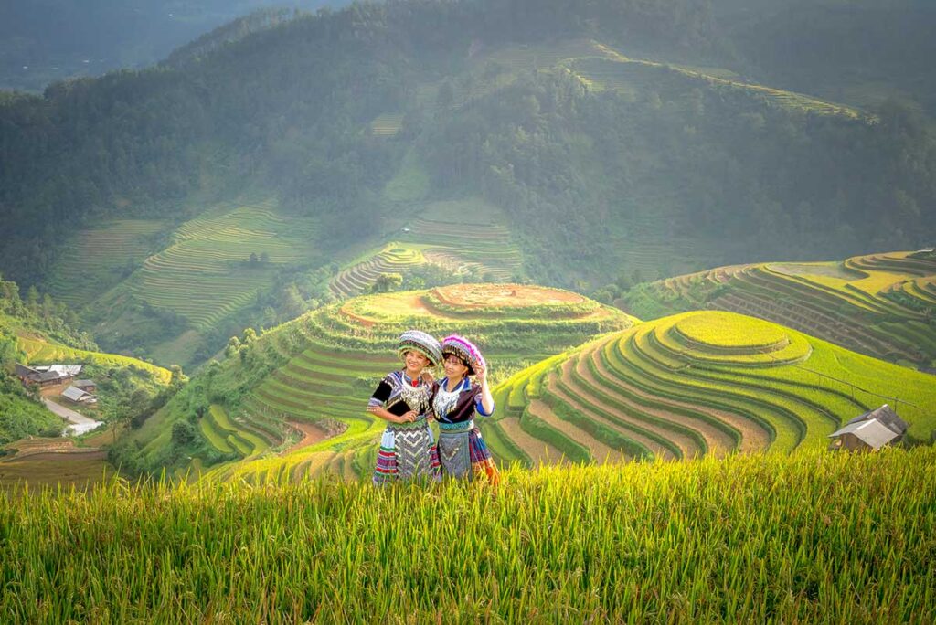Tourists in traditional ethnic clothing posing in front of terraced rice fields in Mu Cang Chai, with layered hills in the background