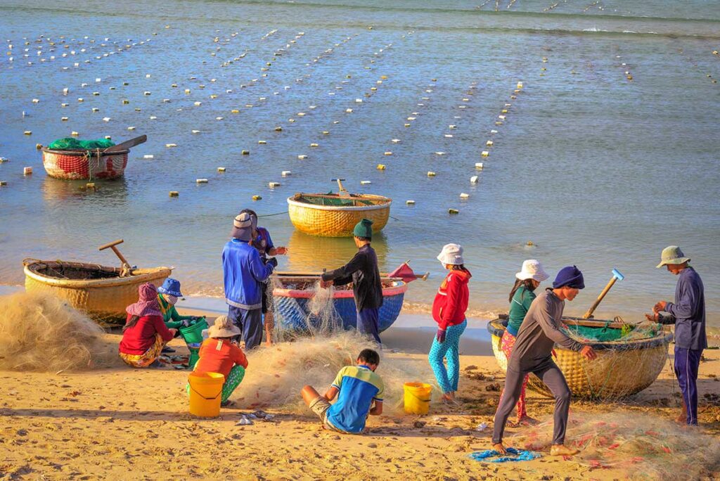 Local fishermen in Ninh Thuan repairing nets beside traditional round basket boats on the sandy shore