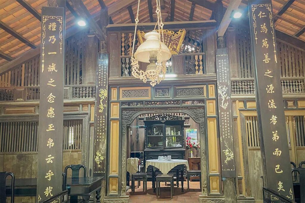 View of the main hall with carved pillars, antique chairs, and a hanging oil lamp in Ong Kiet’s Ancient House, Cai Be – an authentic Mekong Delta architectural gem.