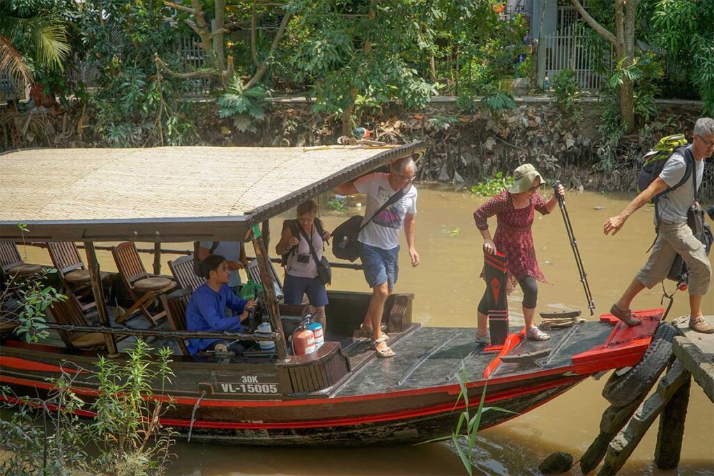 Tourists disembarking from a traditional wooden boat on a canal in Cai Be, Tien Giang – a common Mekong Delta boat tour route linked with Ong Kiet’s Ancient House.