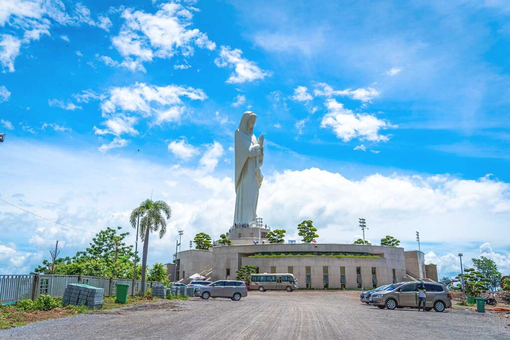 A ground-level view of the Our Lady of Nui Cui statue, taken from the parking area, with the towering monument in the background.