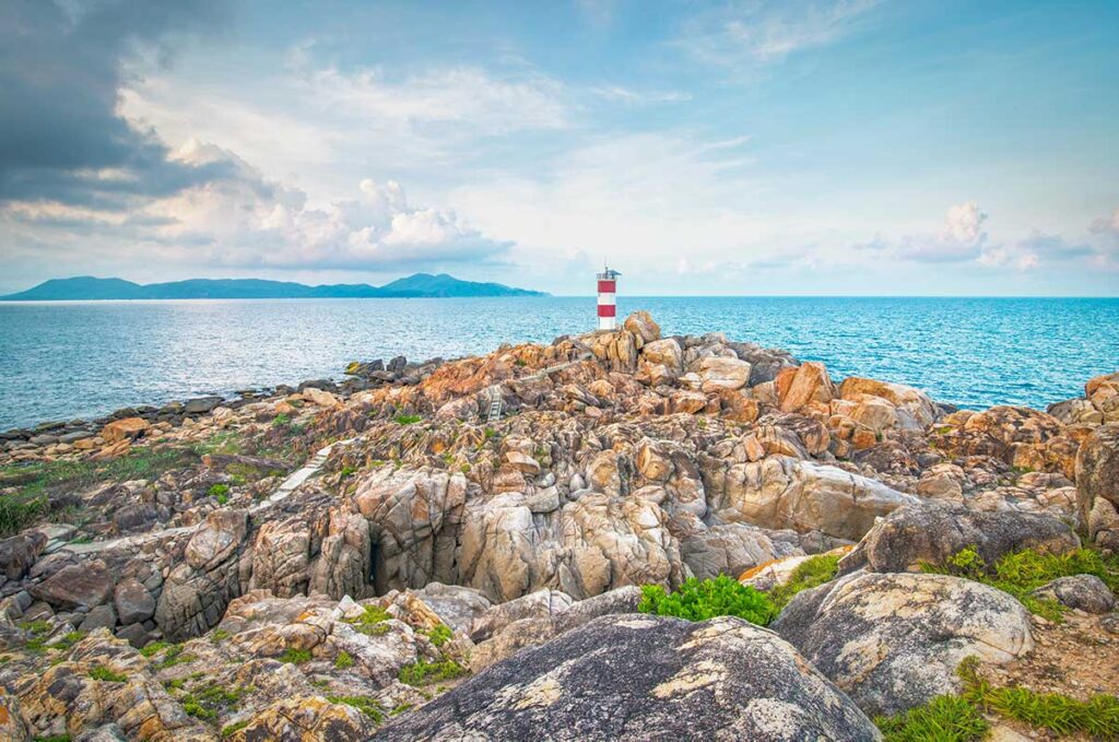 Rocky coastline in Phu Yen with a small lighthouse on a hill, overlooking the sea under a bright blue sky