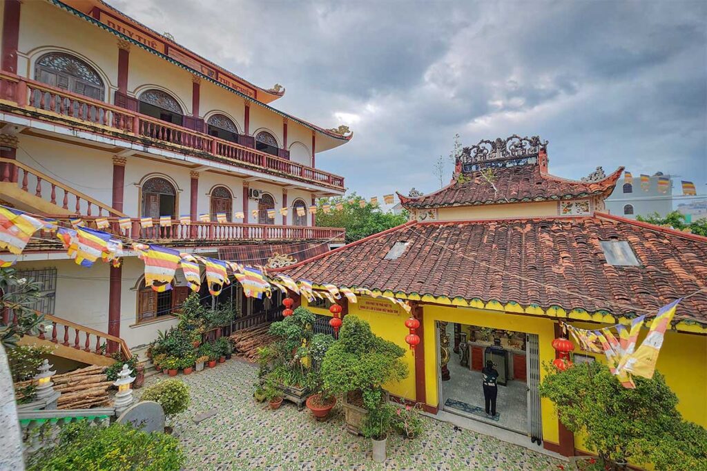 Quan Am Pagoda in Ca Mau featuring yellow walls, tiled roofs, and Buddhist prayer flags in the courtyard.