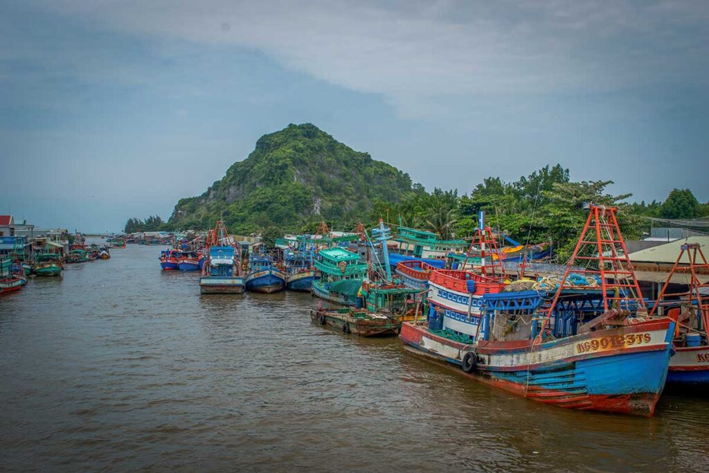 Colorful fishing boats docked at Rach Gia Port with a green hill backdrop – a busy coastal hub in the Mekong Delta’s Kien Giang Province