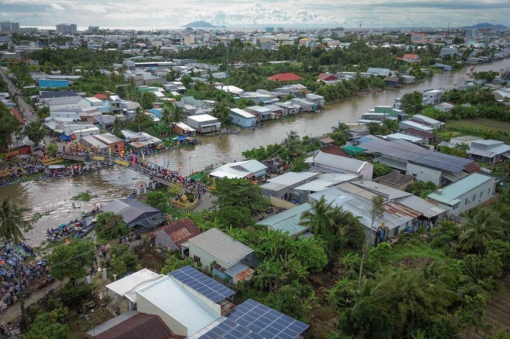 Aerial view of Rach Gia’s canal network during a local event, with residential houses lining the river and a bustling crowd gathering near the waterway.