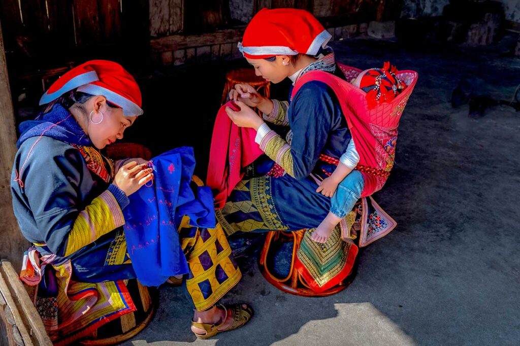 Ethnic minority women in traditional clothing in Sapa sewing colorful fabric by hand inside a local home