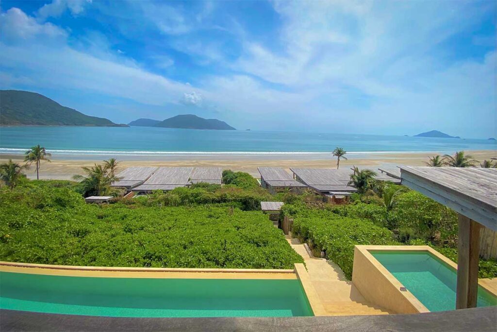 View from Six Senses Con Dao overlooking Dat Doc Beach with private villas, infinity pools, and a long sandy coastline facing the ocean.