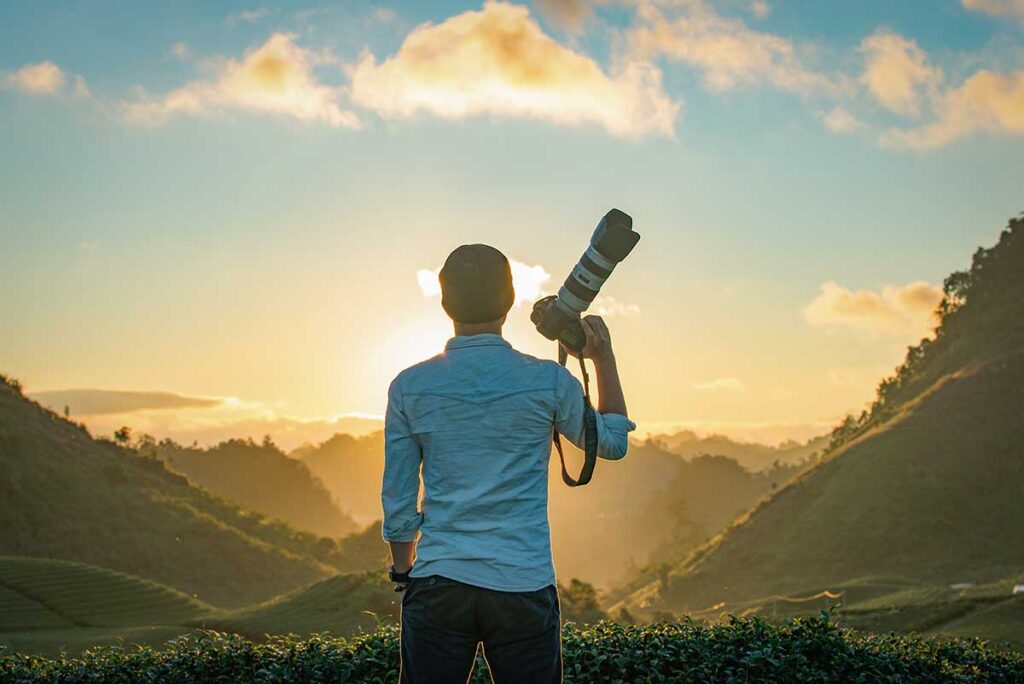 Photographer standing on rolling tea hills in Moc Chau at sunrise, overlooking green plantations and mountain scenery