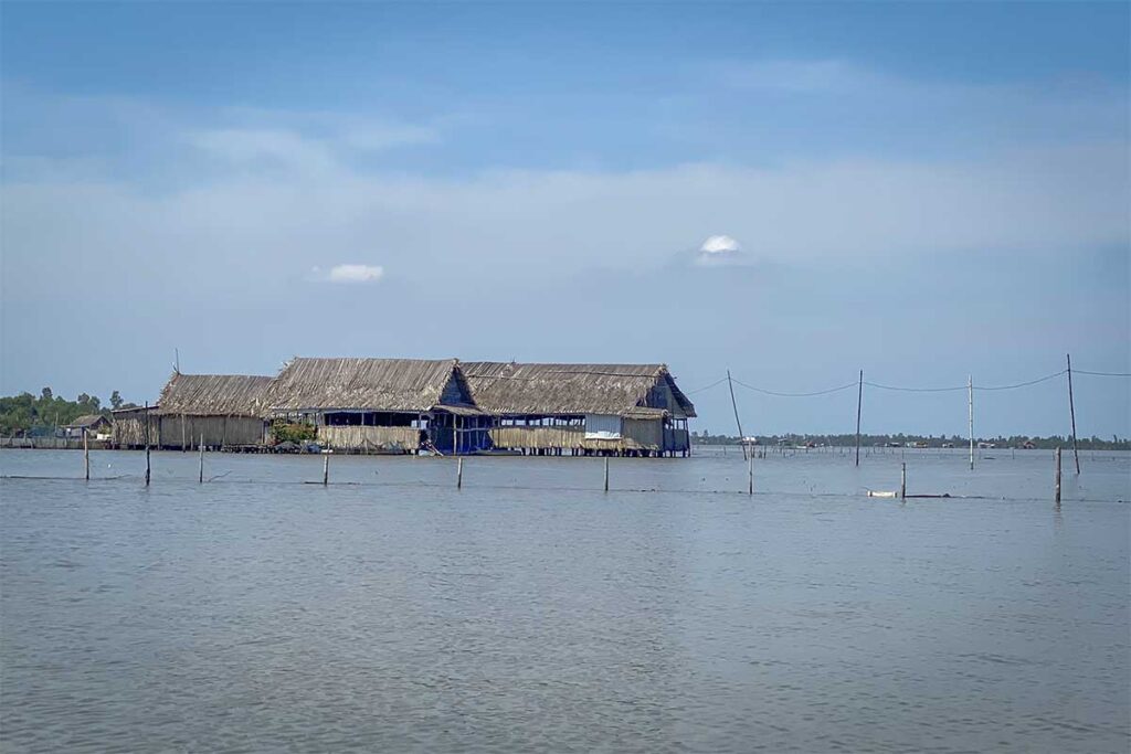 Traditional stilt house on Thi Tuong Lagoon in Ca Mau, Vietnam, built above the water with thatched roofs.