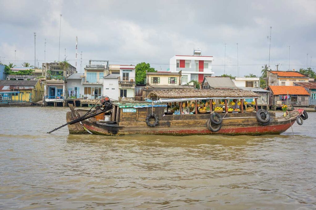 Wooden merchant boat piled with pineapples and produce passing riverside homes at Cai Be floating market in Tien Giang, Mekong Delta.