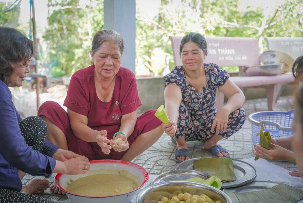 Family preparing traditional rice cakes wrapped in banana leaves during a home cooking session in Tien Giang, showcasing Mekong Delta food culture.
