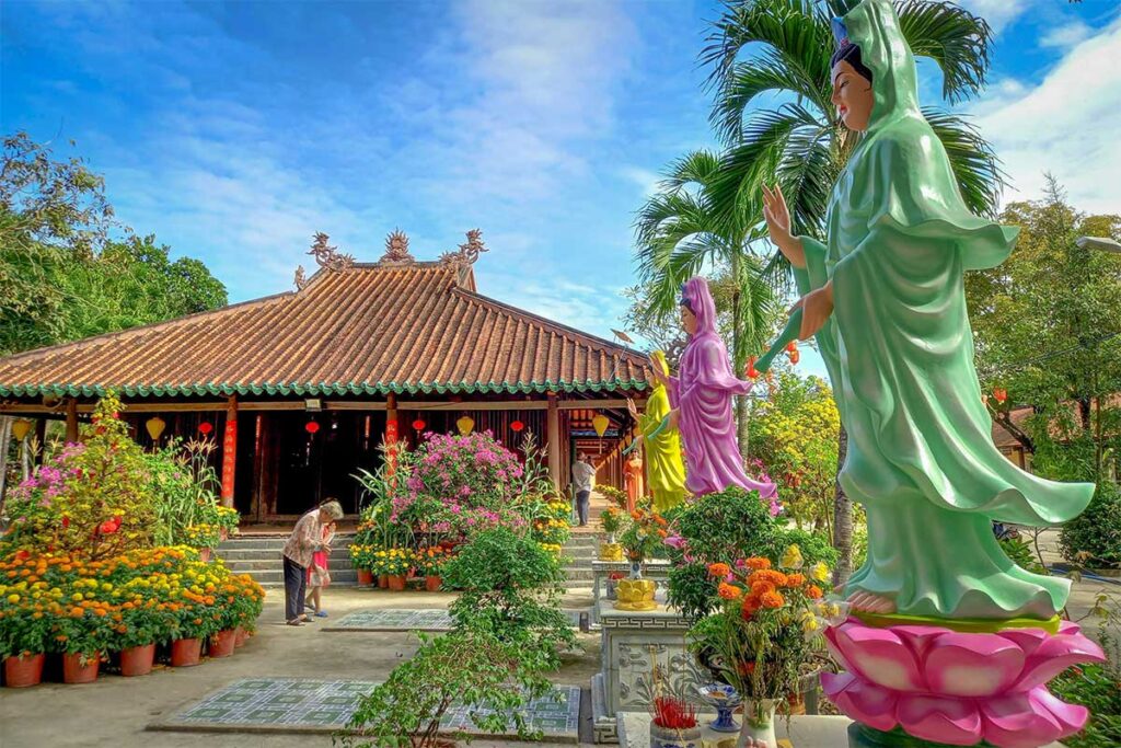 Ton Thanh Pagoda in Long An with colorful Buddha statues and a peaceful courtyard full of potted flowers and tropical plants.