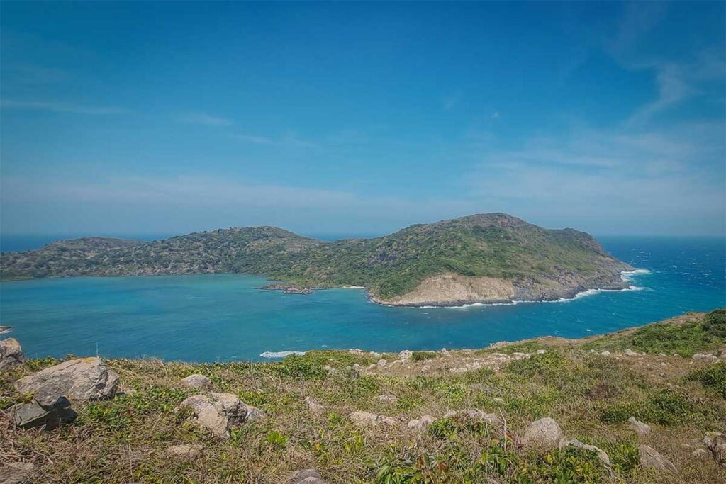 View over Dam Tre Bay in Con Dao National Park, with clear turquoise water, small forested islands, and rocky coastal hills seen from an elevated hiking viewpoint