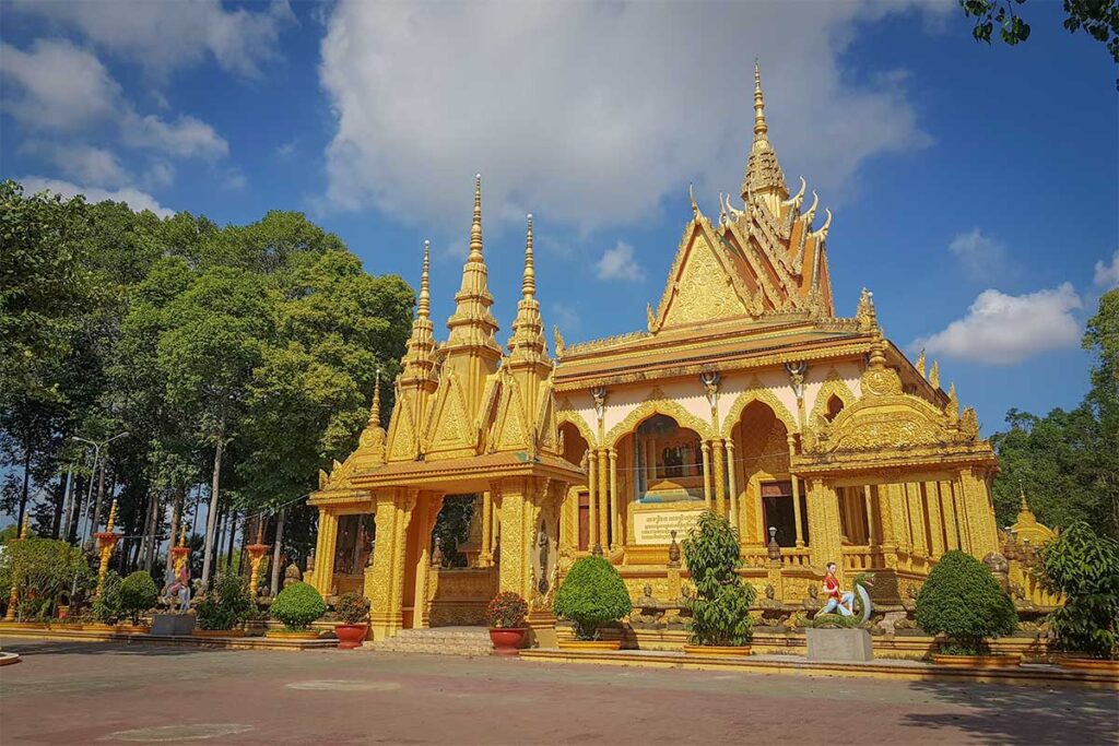 Wide view of the ornately carved golden exterior of Vam Ray Pagoda, one of the most famous Khmer temples in Tra Vinh, set against a clear blue sky.