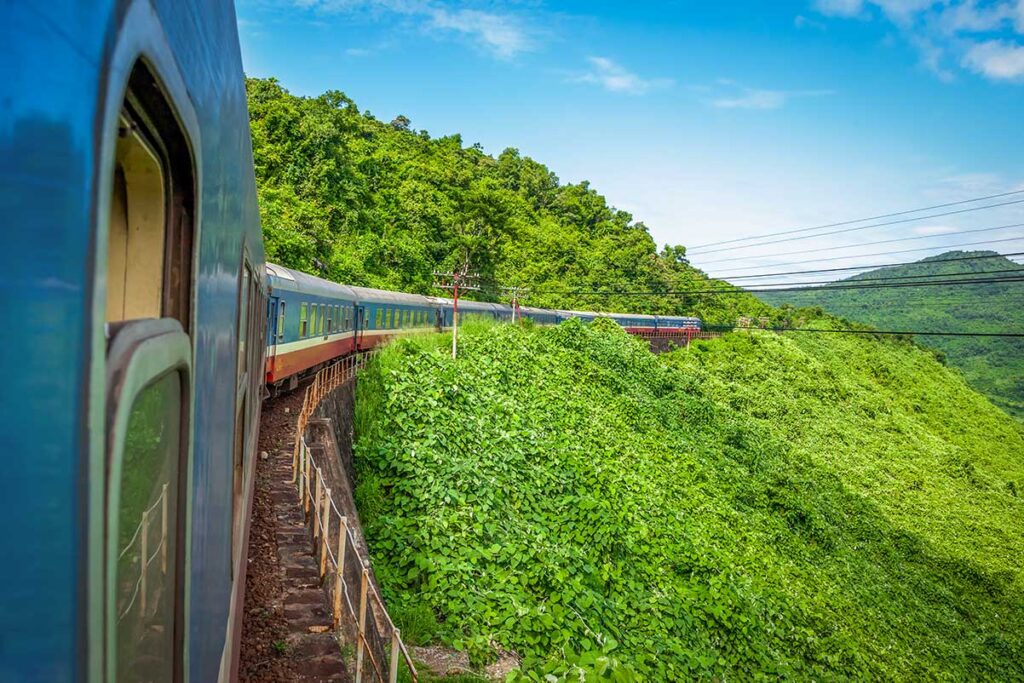 Reunification Express train curving through lush green mountains along the Hai Van Pass, one of the most scenic train routes in Vietnam